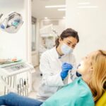 Dentist in mask and gloves examining a patient in a bright dental clinic, leaning over the open mouth treatment in progress at a dental chair
